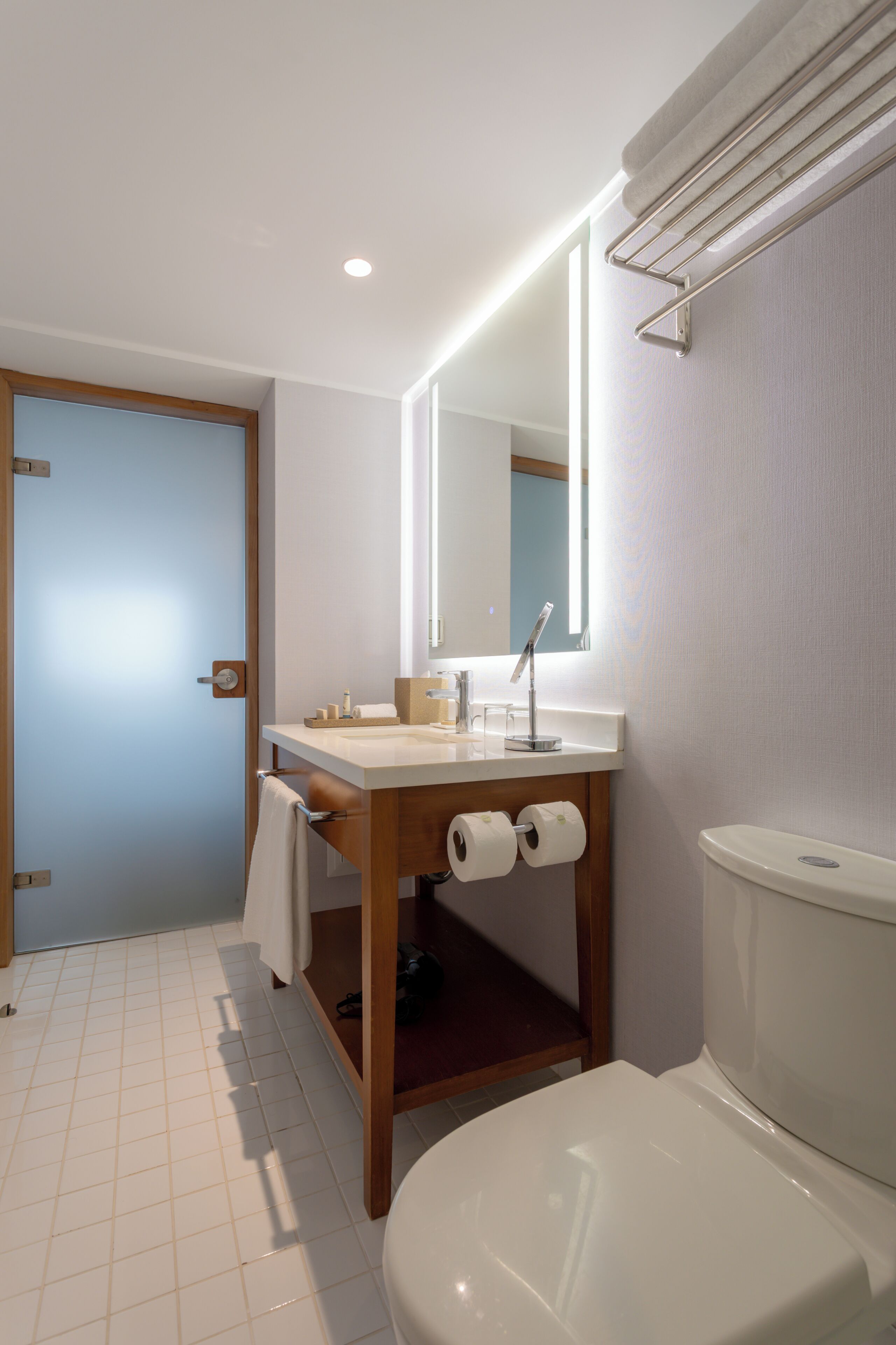 A bathroom with a toilet, sink, mirror, and towel rack.