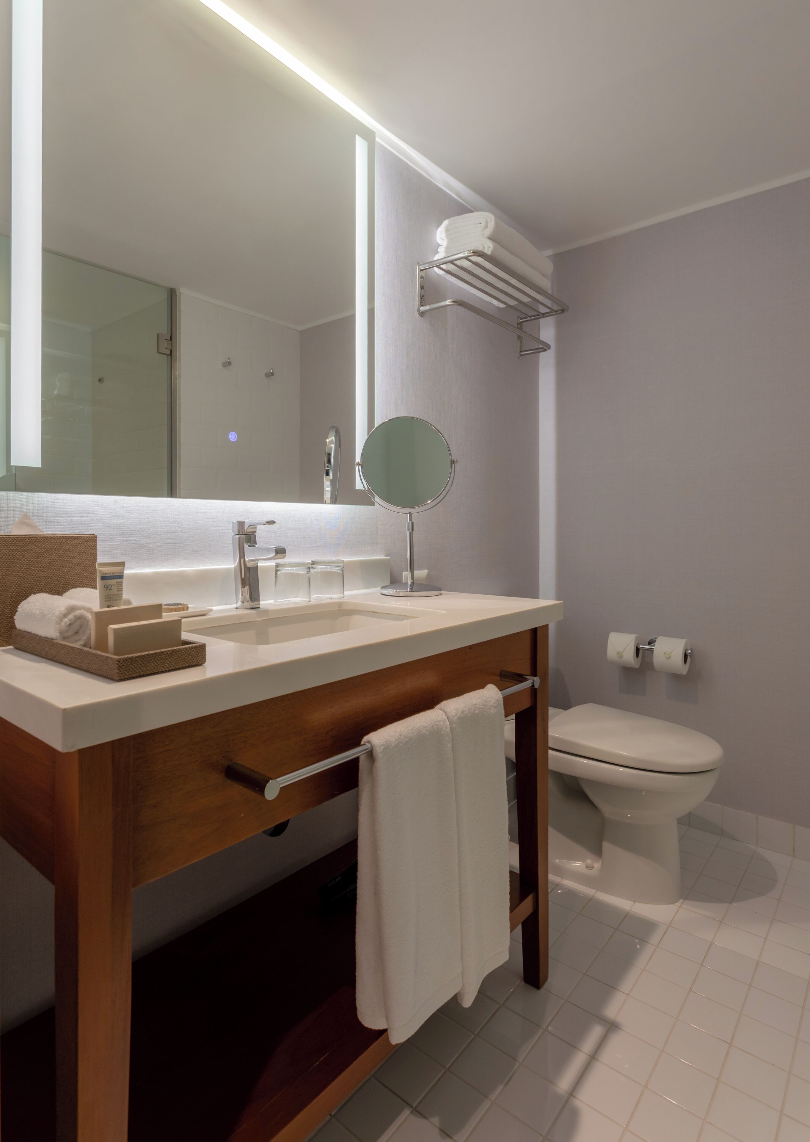 Un baño moderno con tocador de madera, un espejo grande, un inodoro y un perchero para toallas.