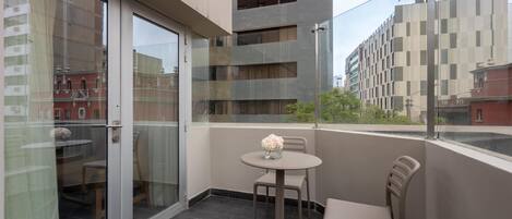 A balcony with a glass door, a round table with chairs, and a vase of flowers.