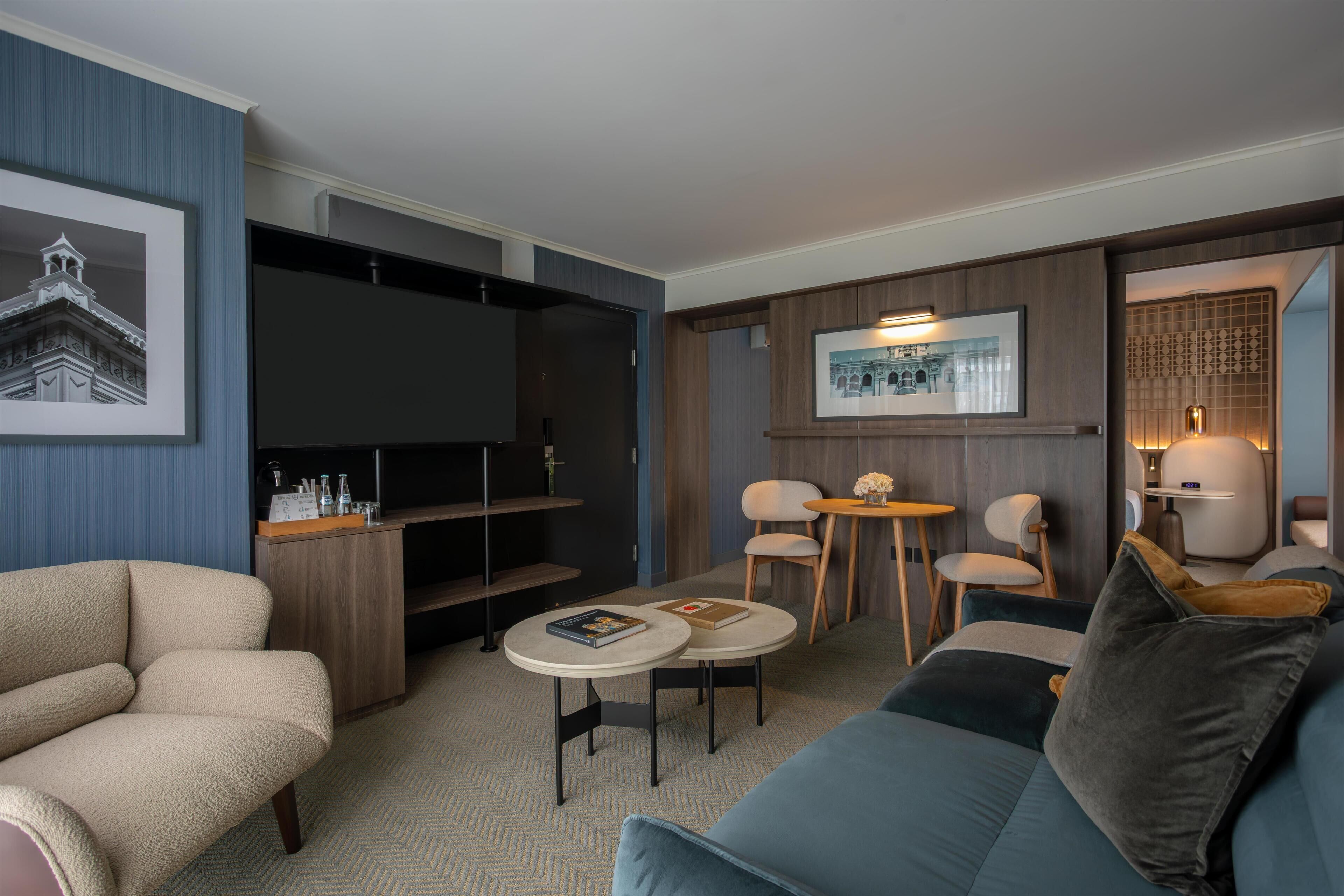Un salon moderne avec un canapé, deux fauteuils, une petite table, un téléviseur et des tableaux encadrés accrochés aux murs.