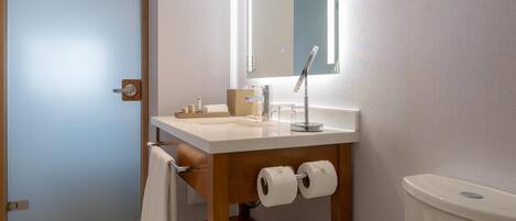 A modern bathroom with a white toilet, a wooden vanity with a mirror, and a towel hanging on the wall.