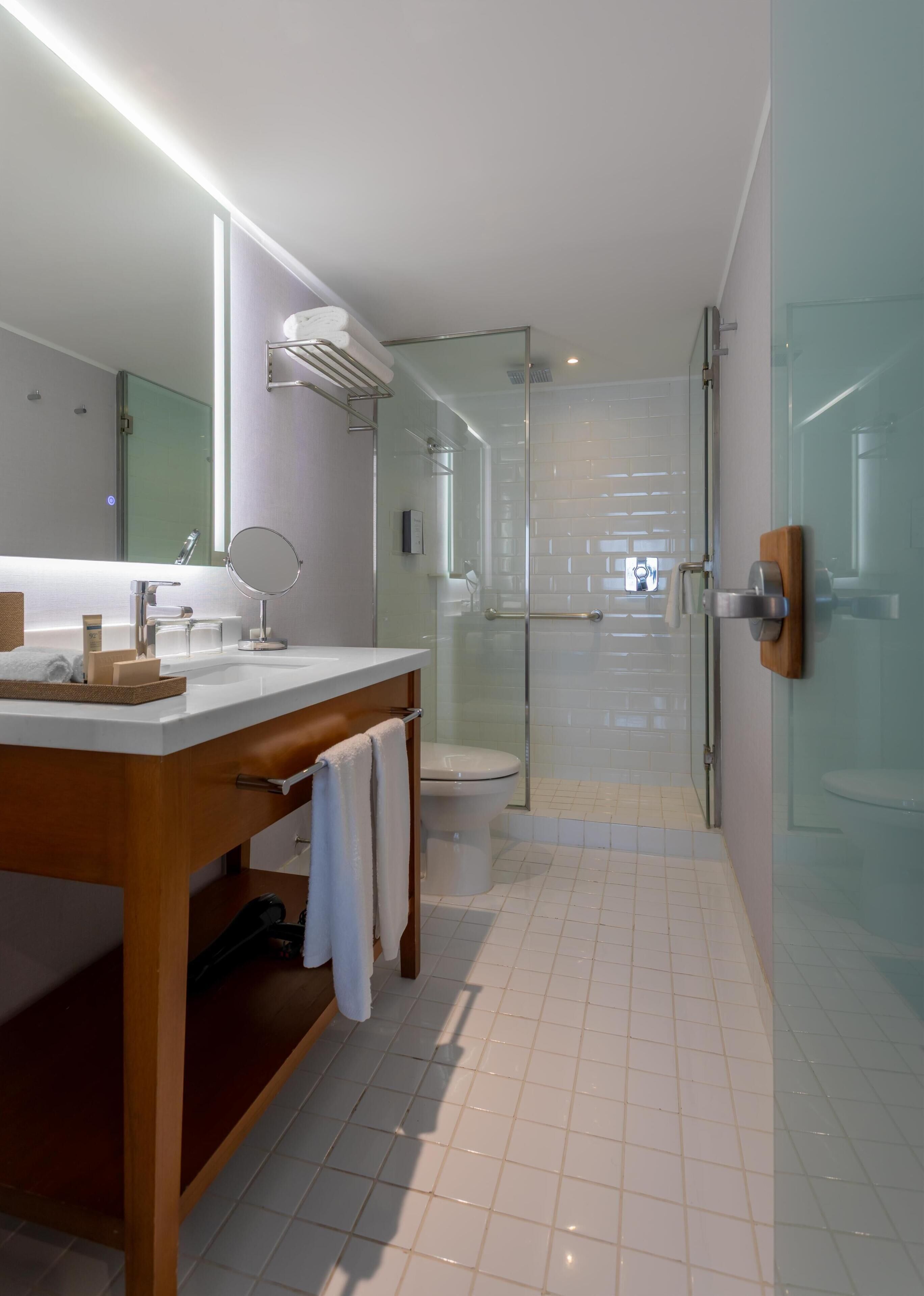 A modern bathroom with a glass shower enclosure, a white sink with a mirror, and a wooden vanity.