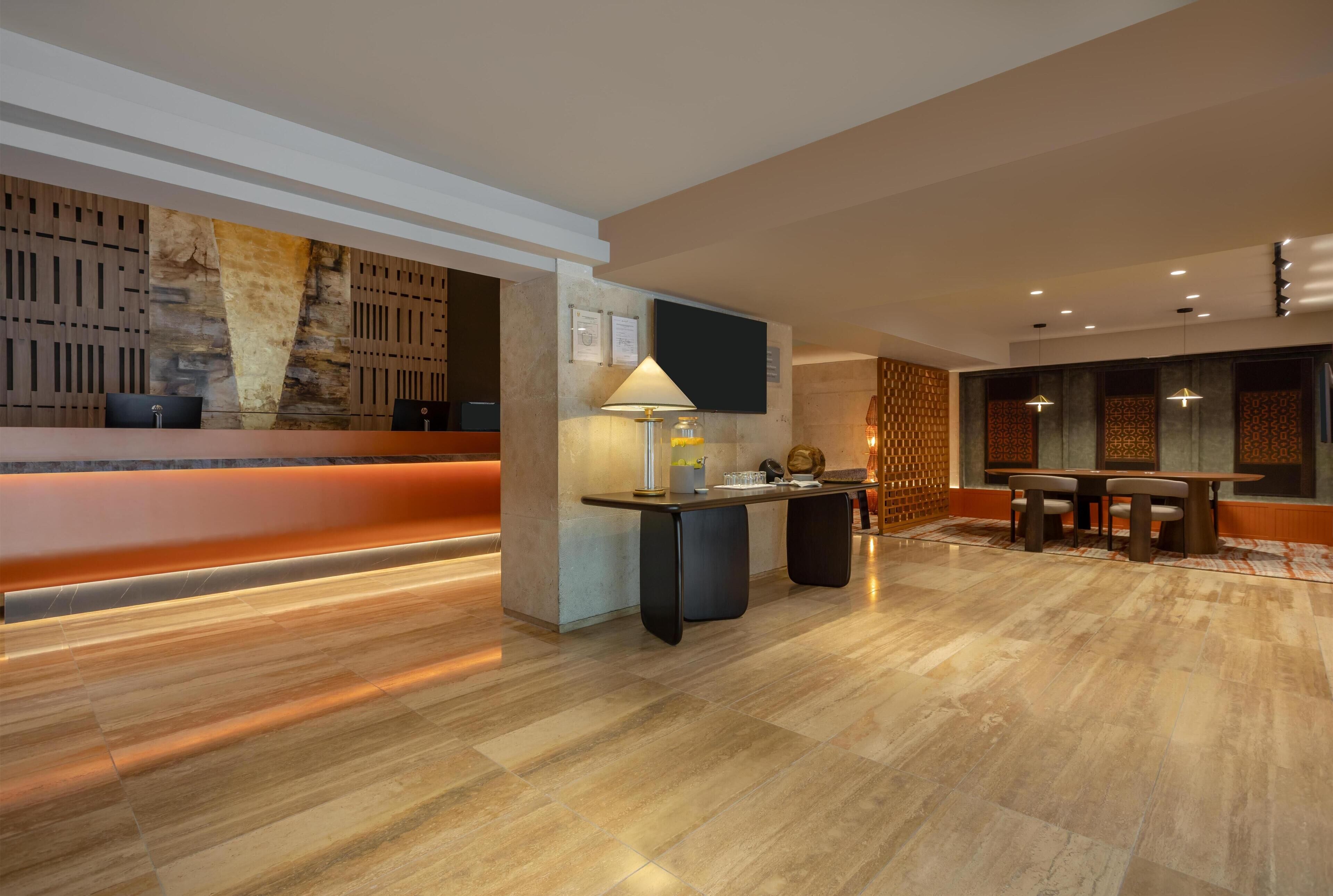 A modern hotel lobby with a reception desk, seating area, and a large wall with a textured design.