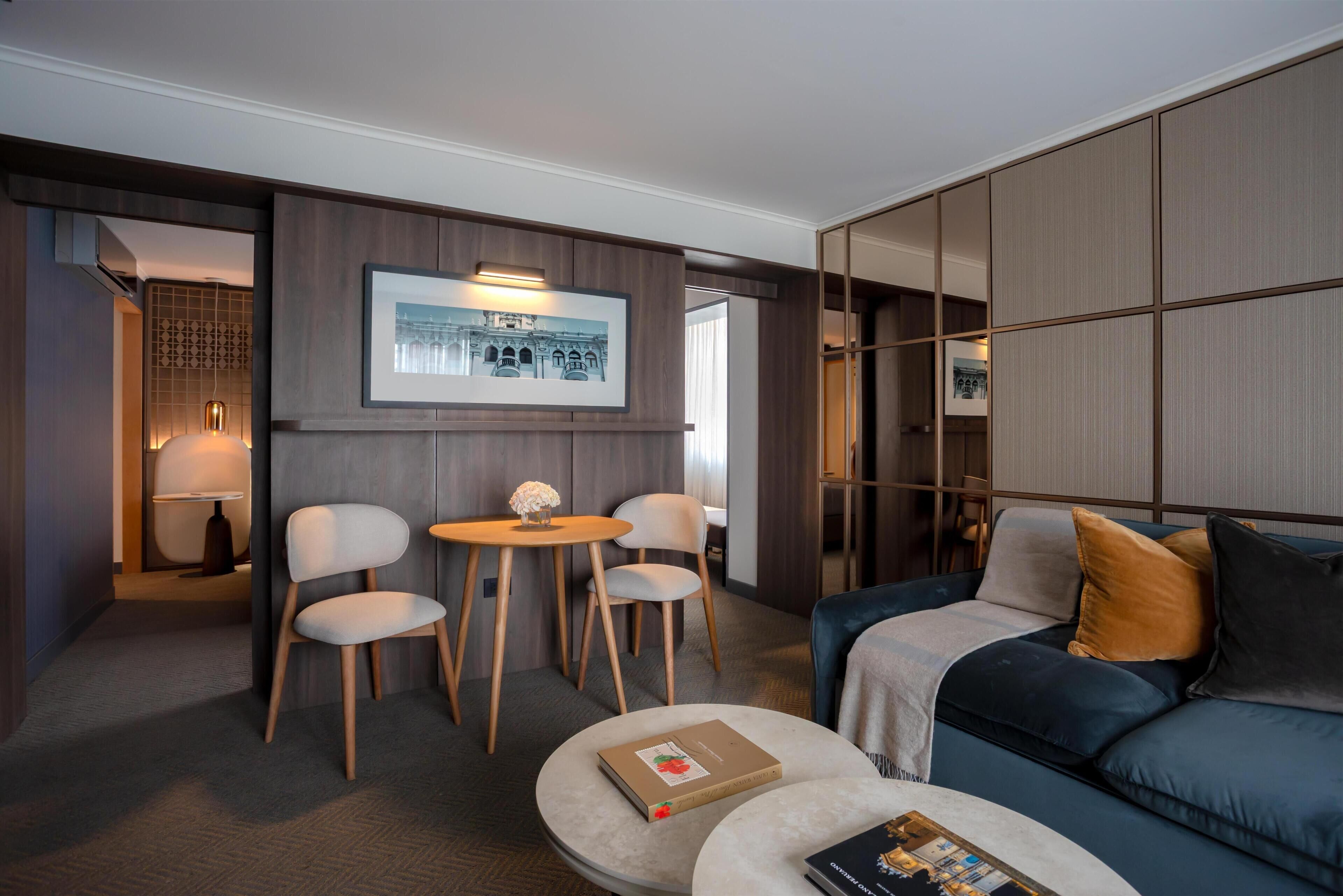 Une chambre d’hôtel moderne avec un canapé bleu, deux fauteuils, une petite table ronde et un tableau encadré au mur.