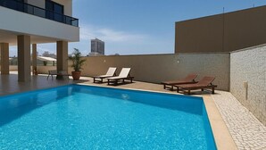 A rectangular swimming pool with clear blue water, surrounded by lounge chairs and a stone wall. - Sea View Apartment in the Heart of Rio Vermelho with Maid (Salvador)