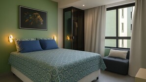 A bedroom with a bed, a nightstand, a wall-mounted lamp, a window with curtains, and a painting on the wall. - Sea View Apartment in the Heart of Rio Vermelho with Maid (Salvador)
