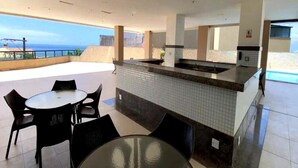 A rooftop bar with a tiled backsplash, a glass-top table, and black chairs. - Sea View Apartment in the Heart of Rio Vermelho with Maid (Salvador)