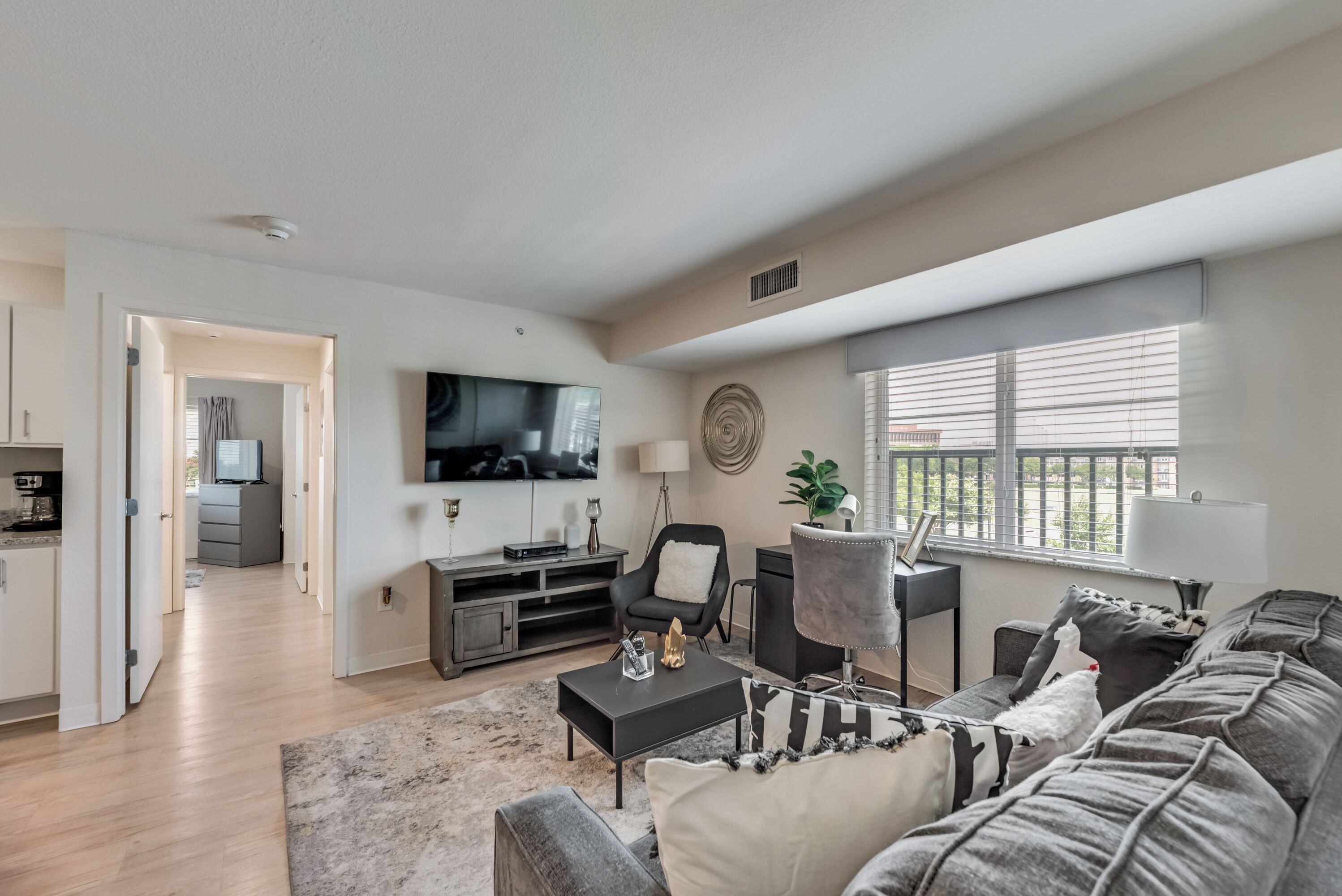 A modern living room with a flat-screen TV, a sofa, a coffee table, and a dining area with a TV and a plant.