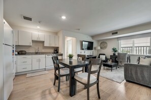 A modern kitchen with white cabinets, a dining table with chairs, a gray sofa, and a TV mounted on the wall. - RD402 - Home|Yard|12mi to Convention Ctr|Sleeps 6 (Richardson)