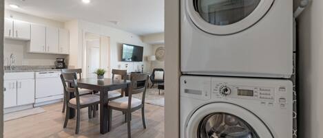 Une cuisine moderne avec des meubles blancs, une table à manger avec des chaises et un lave-linge encastré.
