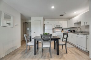 A modern kitchen with white cabinets, a dining table with chairs, and a microwave.