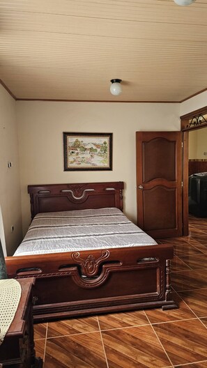 A bedroom with a wooden bed, a framed picture on the wall, and a door to another room.