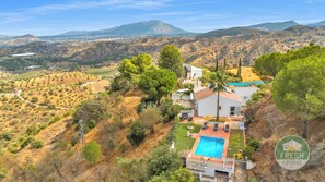 Une maison avec une piscine, entourée d’un paysage vallonné et d’arbres.