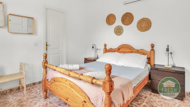 A neatly arranged bedroom with a wooden bed, a bedside table, a nightstand, a chair, and a wall-mounted air conditioner. - Casa del Barco: Villa with Private Retreat Vibes (Guaro)