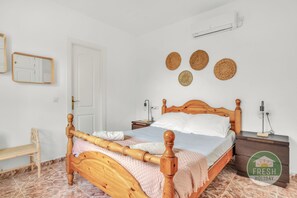 A neatly arranged bedroom with a wooden bed, a bedside table, a nightstand, a chair, and a wall-mounted air conditioner. - Casa del Barco: Villa with Private Retreat Vibes (Guaro)