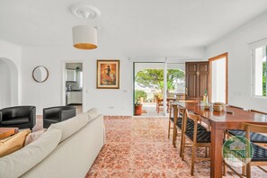 Un salon moderne avec un canapé, des fauteuils, une table à manger et une cuisine en arrière-plan.