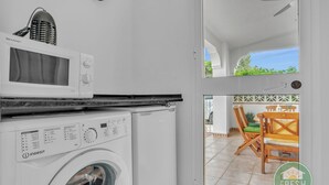 A compact kitchen with a microwave, washing machine, and a dining area visible through a glass door. - Casa del Barco: Villa with Private Retreat Vibes (Guaro)