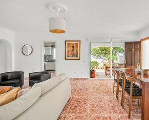 A modern living room with a sofa, chairs, a dining table, and a kitchen in the background. - Casa del Barco: Villa with Private Retreat Vibes (Guaro)