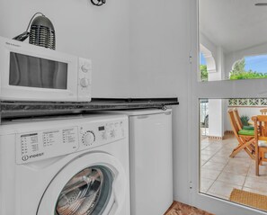 A compact kitchen with a microwave, washing machine, and a dining area visible through a glass door. - Casa del Barco: Villa with Private Retreat Vibes (Guaro)