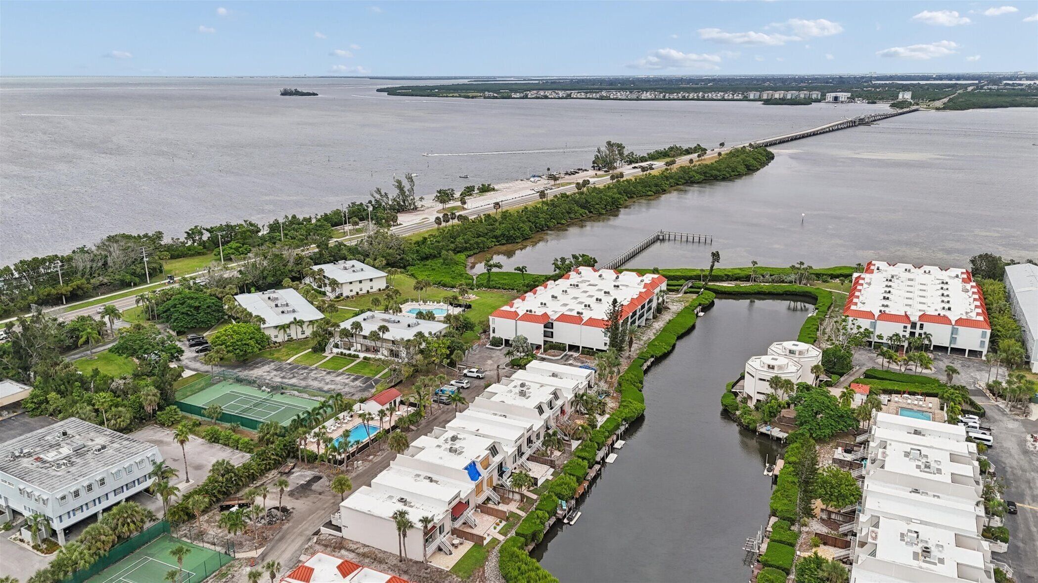 Vista aérea de un hotel costero con varias edificaciones, un puerto deportivo y un puente al fondo.