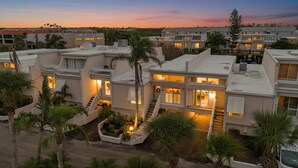 A modern residential complex with multiple two-story buildings, featuring balconies, a central courtyard with palm trees, and a sunset sky. - Coastal Oasis, Lovely 3-bedroom condo with AC in Holmes Beach (FL - Holmes Beach)