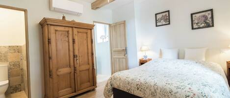 Un dormitorio con un armario de madera, una cama con ropa de cama floral, una araña y dos láminas botánicas enmarcadas en la pared.