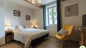 Une chambre à coucher avec un lit, des lampes de chevet, une chaise, un meuble pour la télévision et une fenêtre avec des rideaux.
