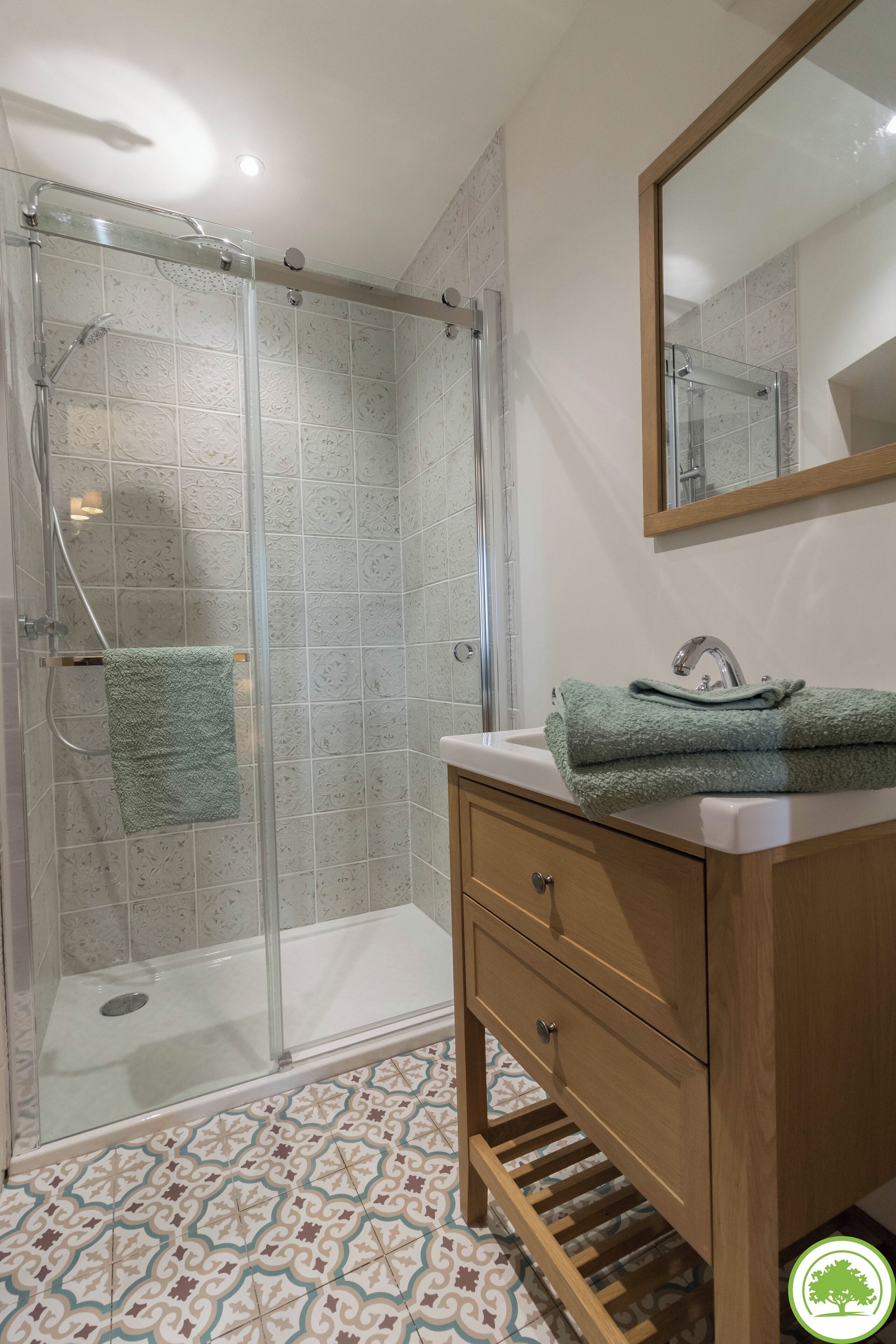 Un bagno con doccia vetro, lavandino con asciugamano verde e mobile contenitore in legno.