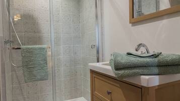 Un bagno con doccia vetro, lavandino con asciugamano verde e mobile contenitore in legno.