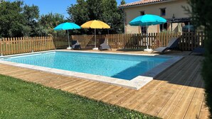Une piscine entourée d’une terrasse en bois et d’une clôture en bois, avec des chaises longues et des parasols à proximité.