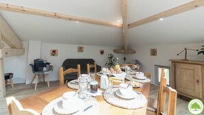 Un coin repas avec une table en bois mise pour le petit-déjeuner, entourée de chaises, avec un canapé et un meuble en arrière-plan.