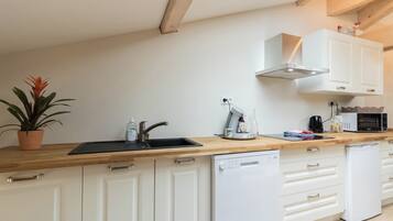 A modern kitchen with white cabinets, a wooden countertop, a dishwasher, a microwave, and a potted plant.