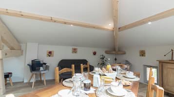 A dining area with a wooden table set for breakfast, surrounded by chairs, with a sofa and a cabinet in the background.