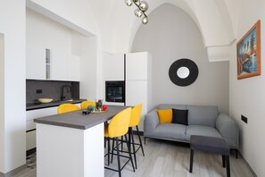 A modern kitchen with a central island, yellow chairs, a grey sofa, and a painting on the wall.