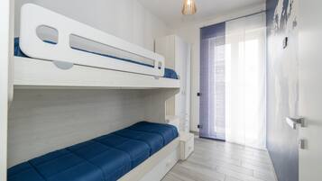 Een kamer met een stapelbed, een klein bureau en een raam met zonwering.