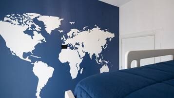Een slaapkamer met een wereldkaart op de muur, een bed met een blauwe deken en een wit hoofdeinde.