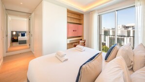 Ein Hotelzimmer mit einem großen Bett, einem Schreibtisch, einem Sessel, einem Fernseher und einem Balkon mit Blick auf die Stadt.