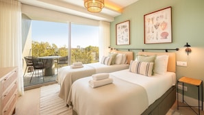 Ein Hotelzimmer mit zwei Betten, einem Balkon mit Tisch und Stühlen sowie Bildern an den Wänden.