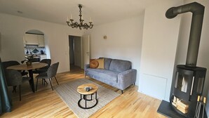 A modern living room with a sofa, a dining table with chairs, a coffee table, and a wood-burning stove. - Almrose Zauber, vacation apartment in the mountains near the ski slopes (Oberau)