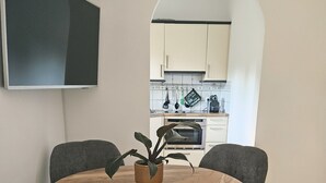 A dining area with a round wooden table, four grey upholstered chairs, a potted plant, and a kitchen visible through an archway. - Almrose Zauber, vacation apartment in the mountains near the ski slopes (Oberau)