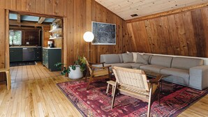 Ein Holzinnenraum mit einer Couch, Sesseln, einem Teppich und einem Wandbild.