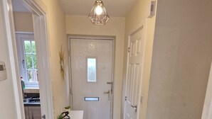 A hallway with a wooden floor, a white door at the end, and a small table with a plant. - NightRest Homes Orchid2 NEC Free Parking  2Toilets (West Midlands)