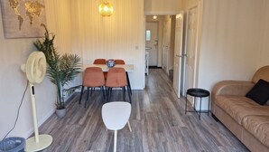 A modern living room with a dining area, a sofa, a floor fan, and a potted plant. - NightRest Homes Orchid2 NEC Free Parking  2Toilets (West Midlands)