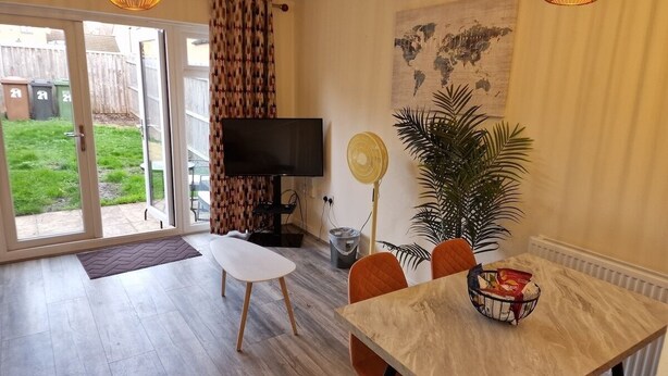 A dining area with a table, chairs, a television, and a fan. - NightRest Homes Orchid2 NEC Free Parking  2Toilets (West Midlands)