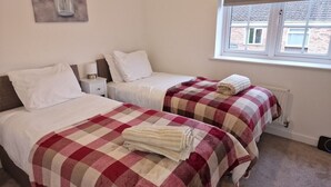A bedroom with two beds, each with a checkered bedspread, a nightstand, a lamp, and a window with a view of buildings outside. - NightRest Homes Orchid NEC Free Parking  2 Toilets (West Midlands)