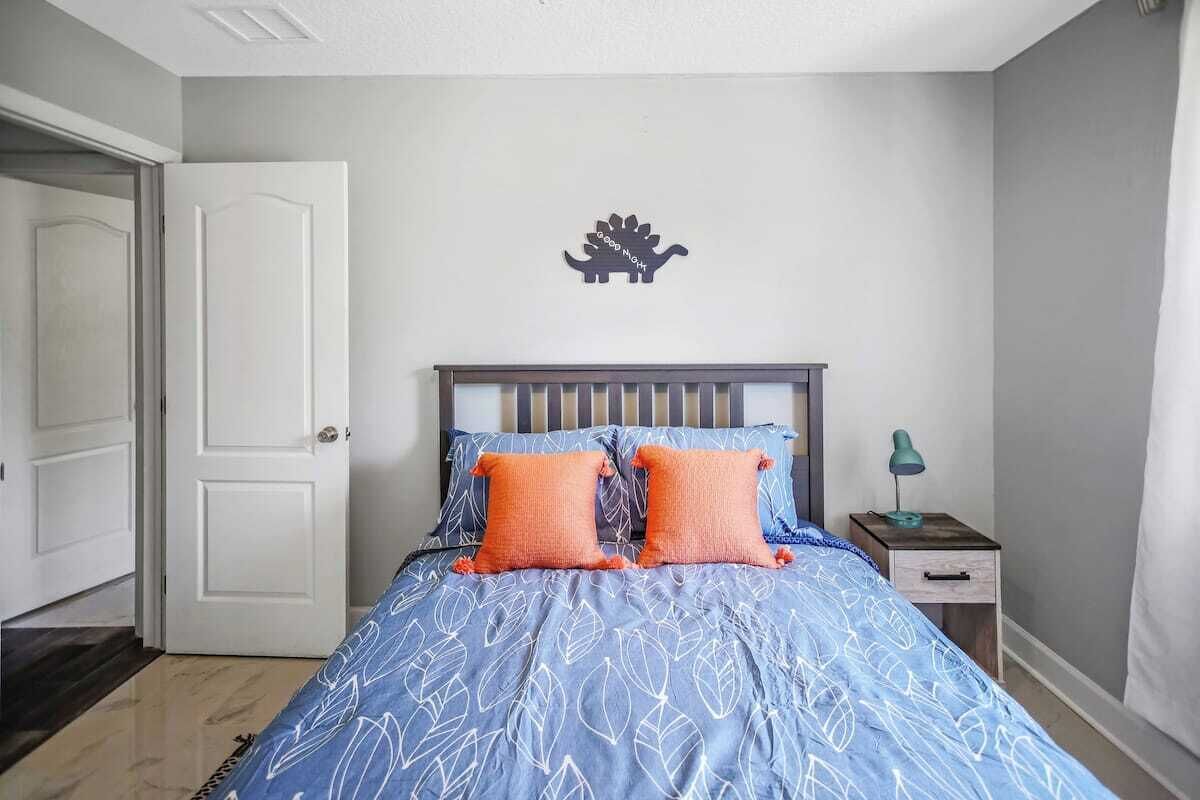 A bedroom with a bed, two pillows, a nightstand, a lamp, and a door.