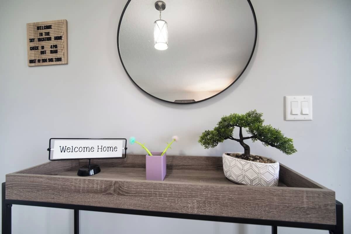 A reception desk with a "Welcome Home" sign, a bonsai tree, and a modern light fixture.