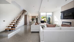 A modern interior with a staircase, white sofas, and a kitchen area.