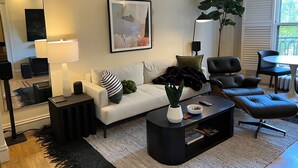 A modern living room with a white sofa, black leather chairs, a coffee table, and a large plant. - Elegant Mid-Century Modern Condo — Fully Furnished Luxury in the Heart of Boston (Boston)