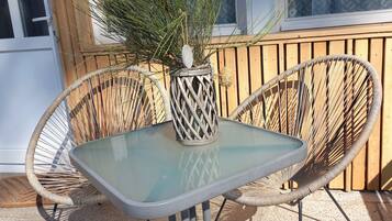 Eine Terrasse mit einem Glastisch, zwei Korbstühlen, einer Ziervase und einem Holzzaun im Hintergrund.